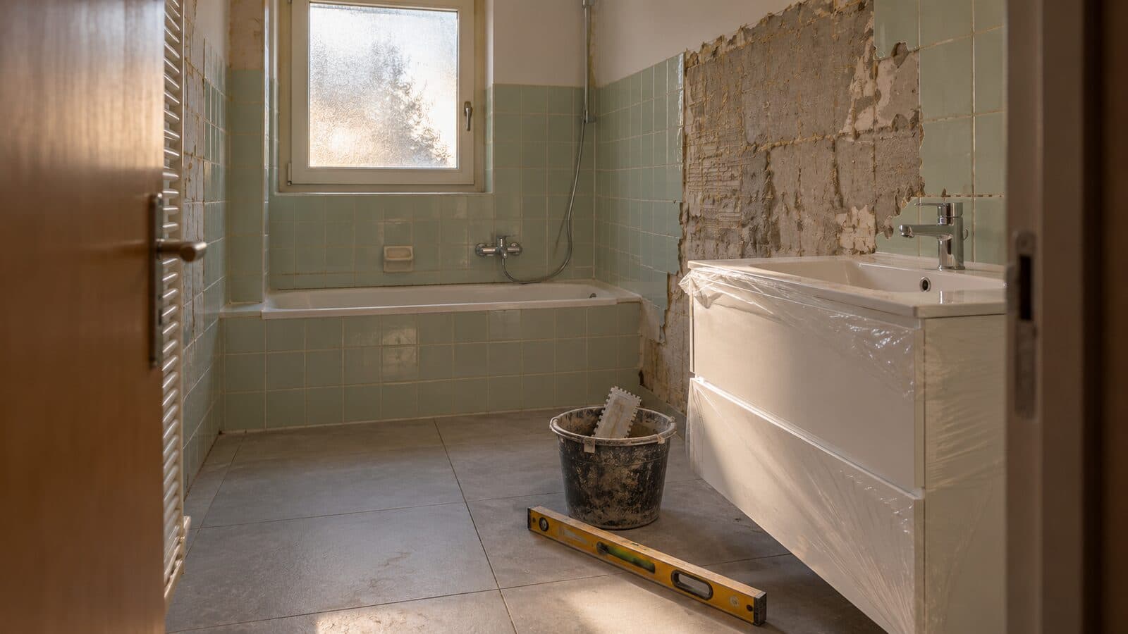 Badezimmer renovieren: Bad mitten in der Renovation mit teils abgeschlagenen Wandplatten, neuem Lavabo in Schutzfolie und grossformatigen Platten am Boden